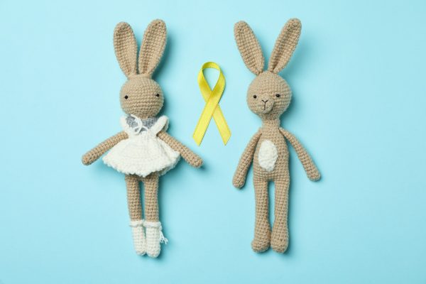 Toy bunnies and childhood cancer awareness ribbon on blue background